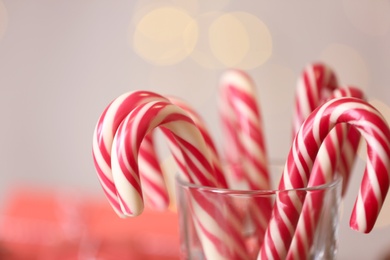 Photo of Christmas candy canes in glass against blurred lights, closeup