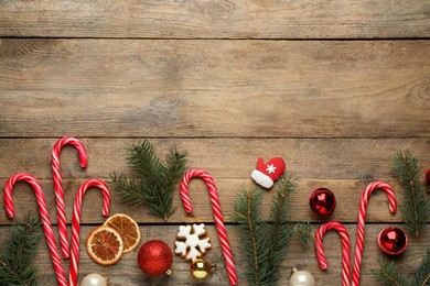 Photo of Flat lay composition with tasty candy canes and Christmas decor on wooden table, space for text