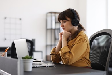 Photo of Woman in headphones watching webinar at table in office