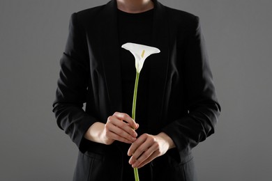 Woman with calla lily flower on grey background, closeup. Funeral ceremony