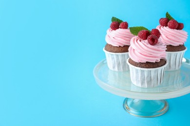 Photo of Delicious cupcakes with cream and raspberries on light blue background, space for text