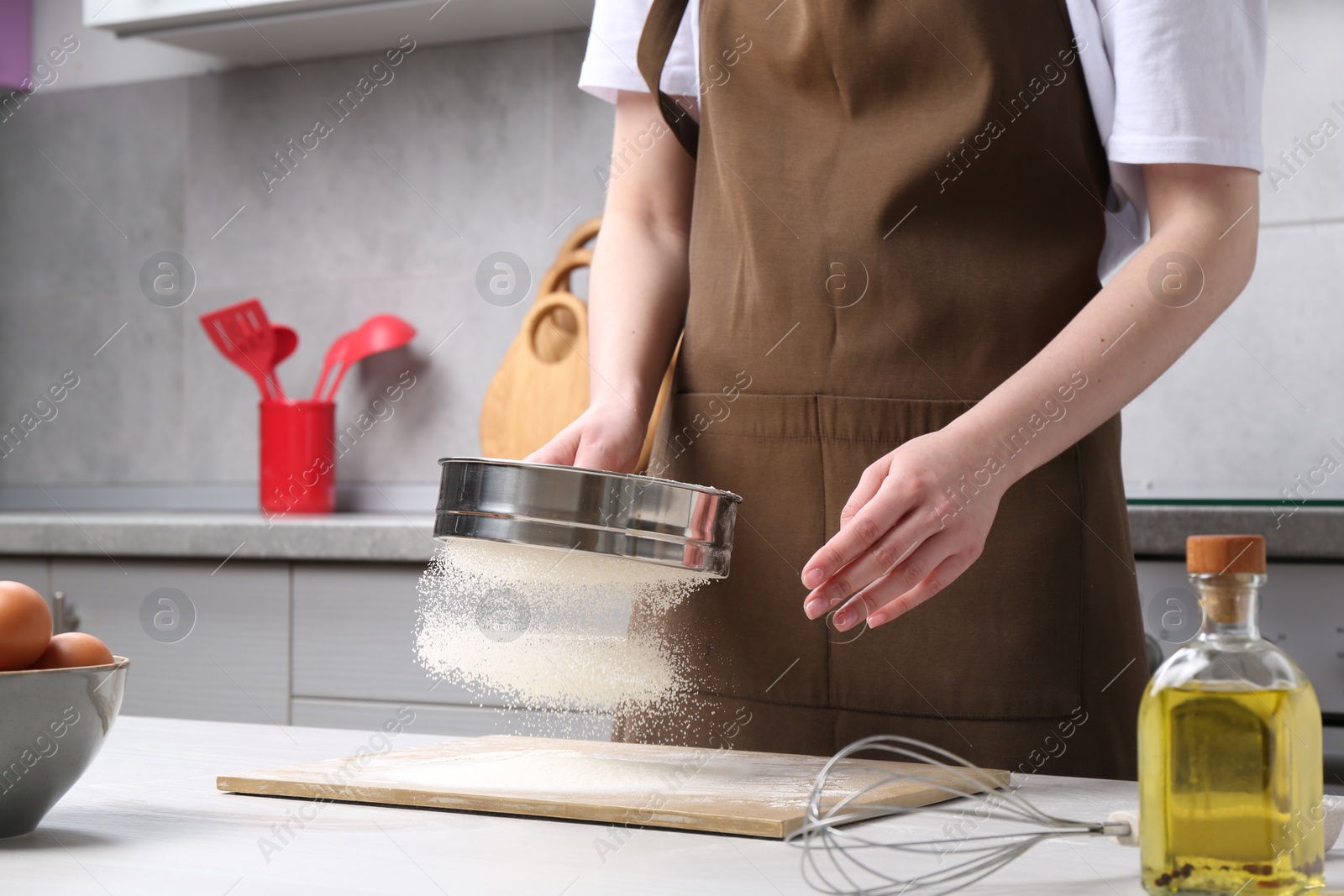 Photo of Woman sieving flour at table in kitchen, closeup