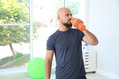 Tired overweight man drinking water in gym