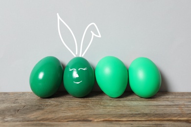 Image of One egg with drawn face and ears as Easter bunny among others on wooden table against light grey background