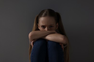 Photo of Sad girl sitting near dark grey background