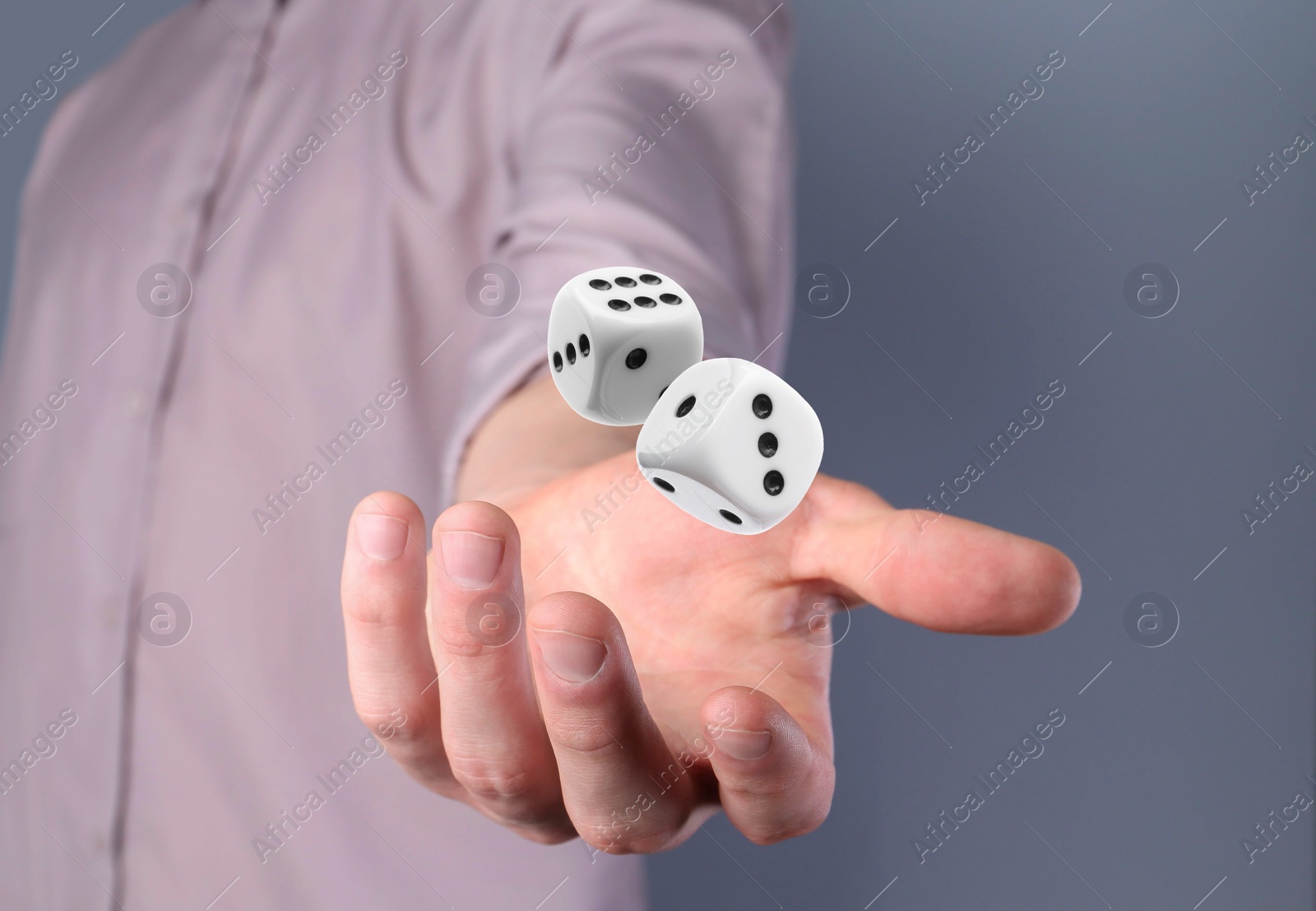 Image of Man throwing white dice on grey background, closeup