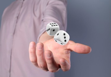 Man throwing white dice on grey background, closeup