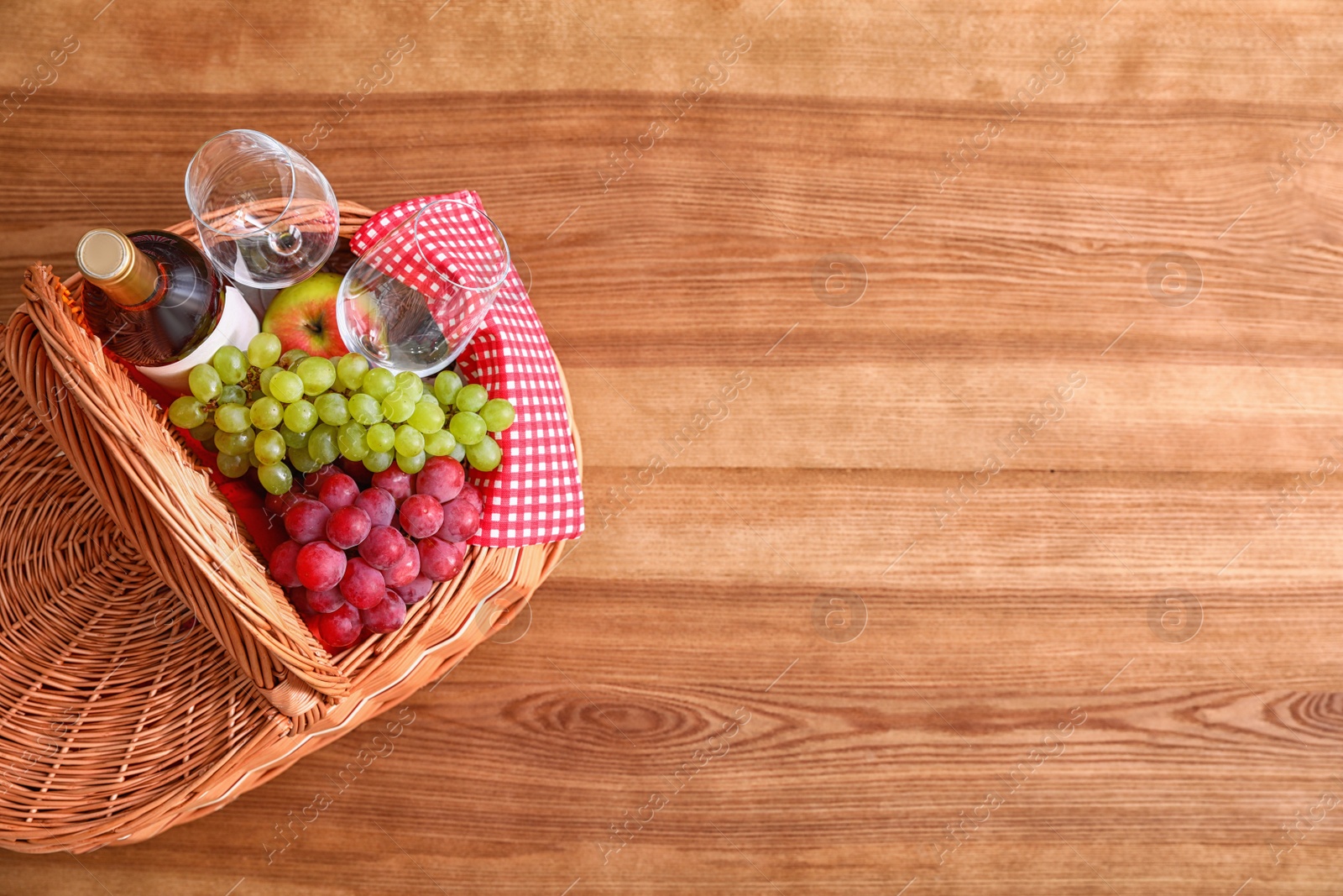 Photo of Picnic basket with wine, glasses and grapes on wooden table, top view. Space for text