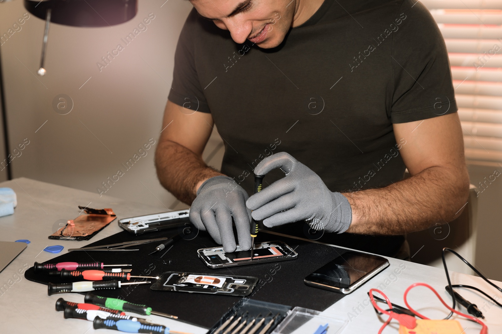 Photo of Technician repairing broken smartphone at table indoors, closeup