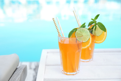 Photo of Refreshing cocktail in glasses near outdoor swimming pool on sunny day. Space for text