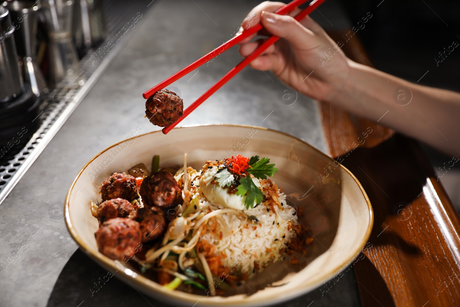 Photo of Woman eating rice and meatballs with chopsticks at table, closeup