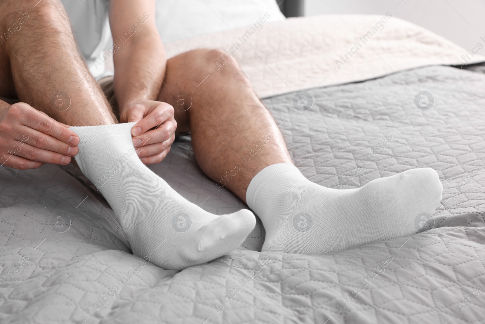 Photo of Man putting on white socks at home, closeup