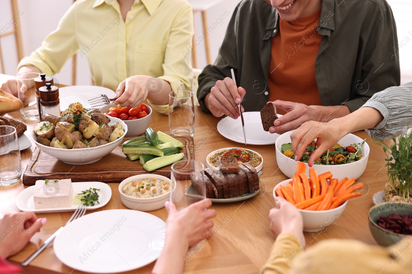 Photo of Friends eating vegetarian food at wooden table indoors, closeup