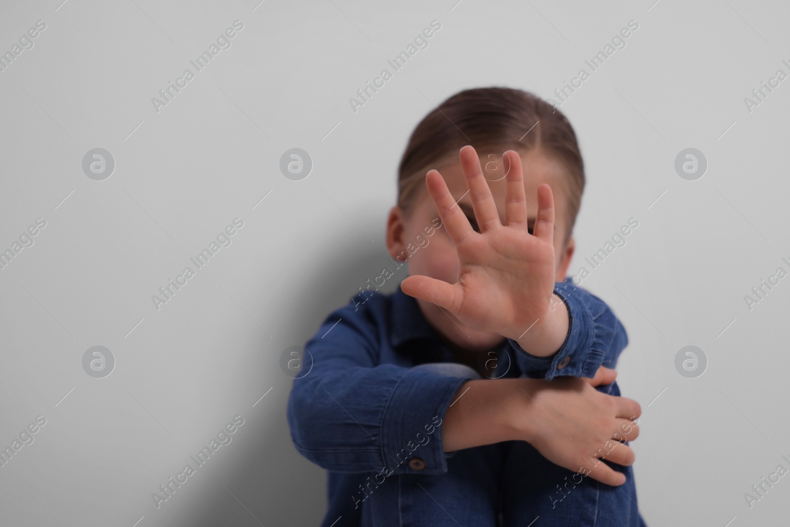 Photo of Child abuse. Girl making stop gesture near grey wall, selective focus. Space for text