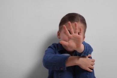 Photo of Child abuse. Girl making stop gesture near grey wall, selective focus. Space for text