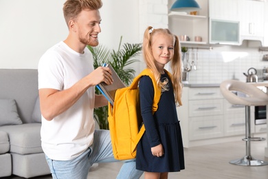 Happy father putting textbooks into little child's school bag at home