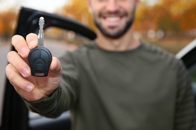 Photo of Young man holding car key near auto, closeup. Driving license test