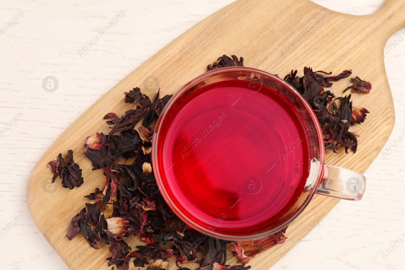 Photo of Cup of fresh hibiscus tea and dry flower leaves on wooden table, flat lay