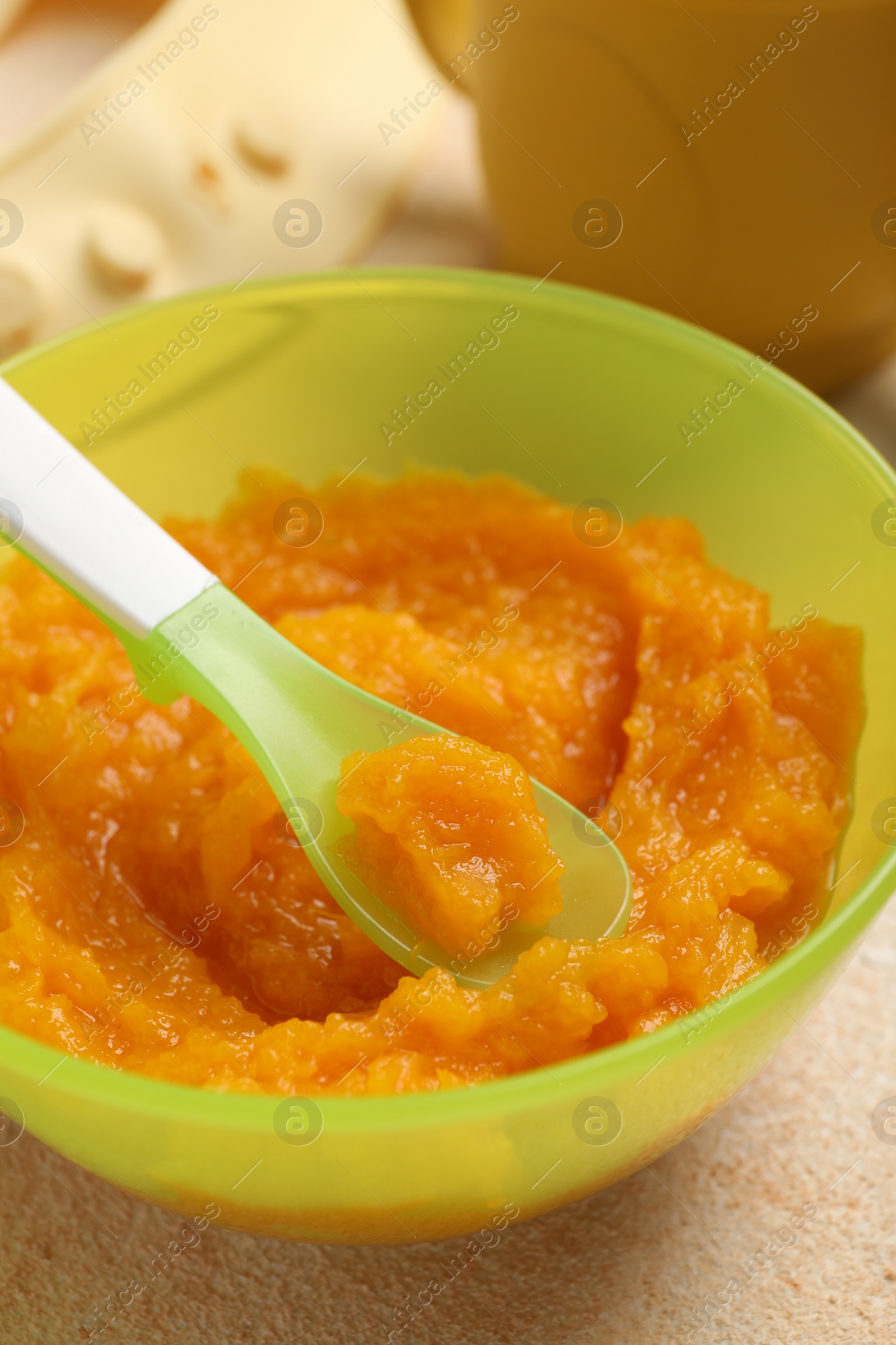 Photo of Baby food. Bowl with tasty pumpkin puree on beige textured table, closeup