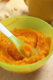 Photo of Baby food. Bowl with tasty pumpkin puree on beige textured table, closeup