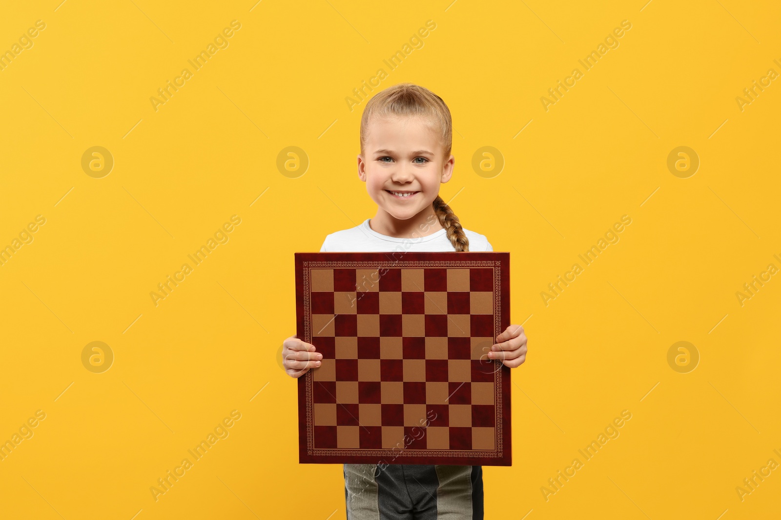 Photo of Cute girl holding chessboard on orange background