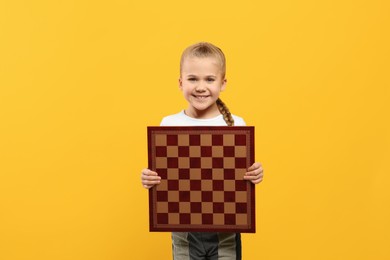 Cute girl holding chessboard on orange background