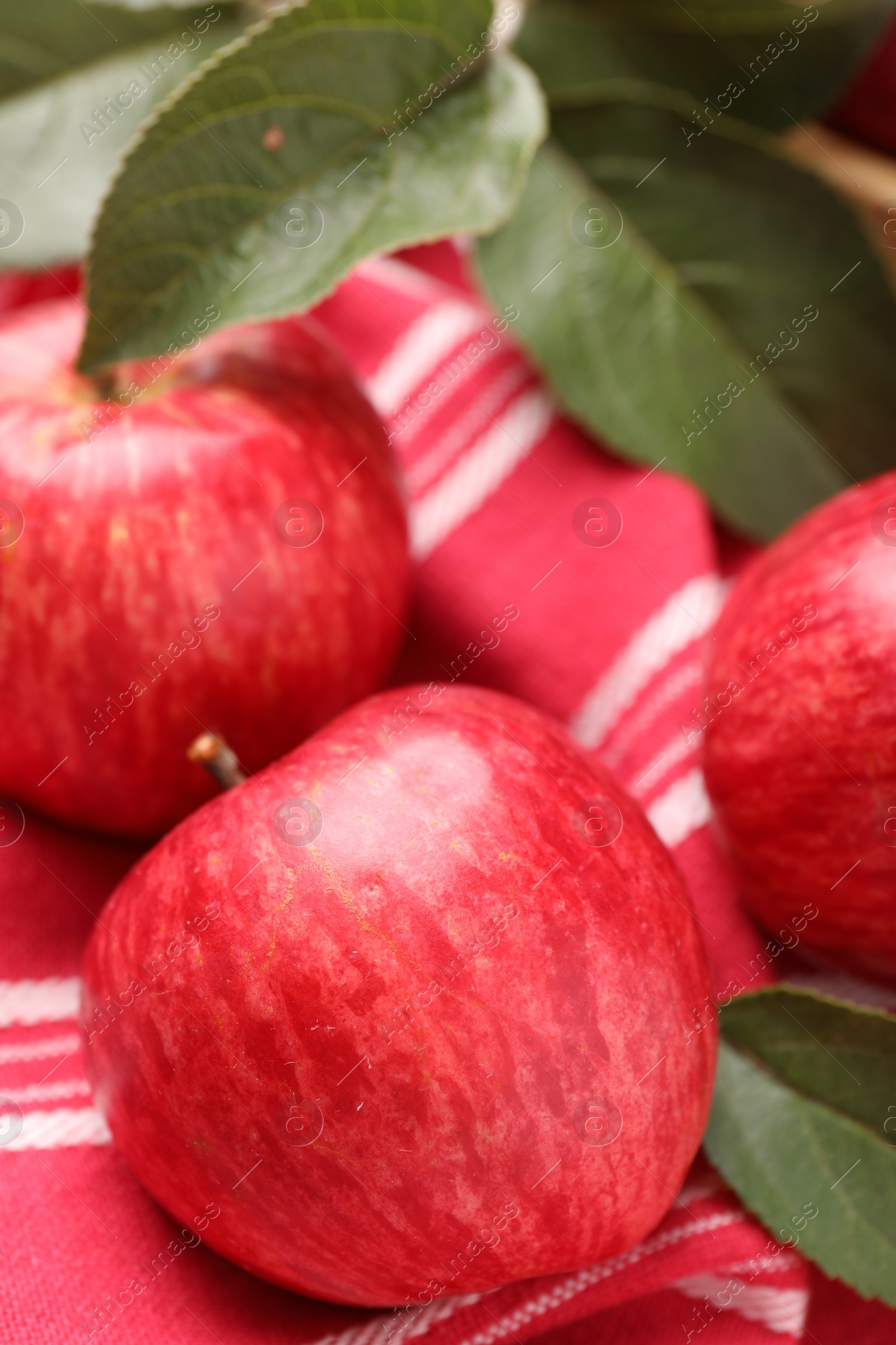 Photo of Fresh red apples with leaves on red cloth, closeup