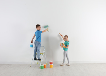 Photo of Little children painting on blank white wall indoors