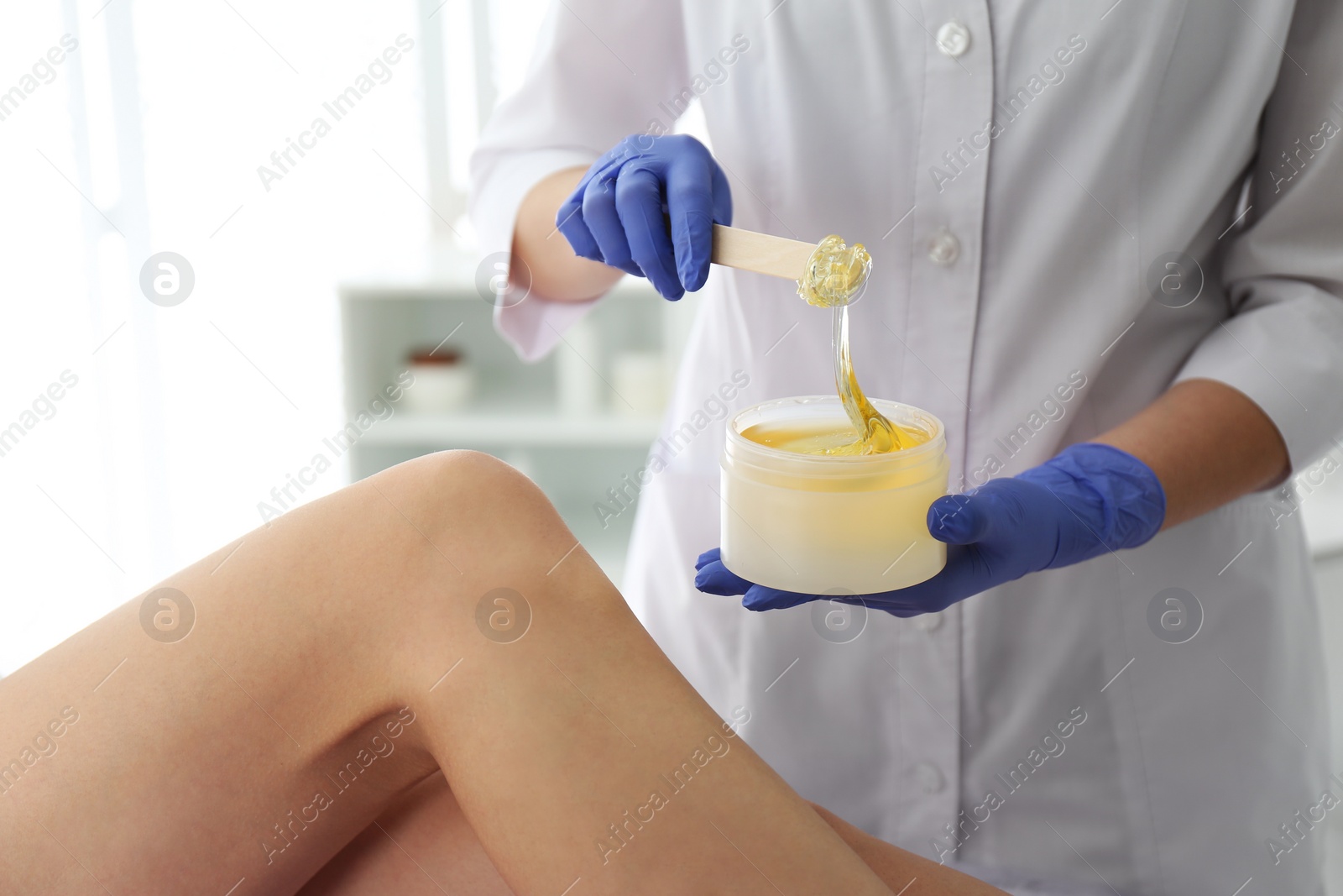 Photo of Woman getting wax epilation of legs in salon, closeup