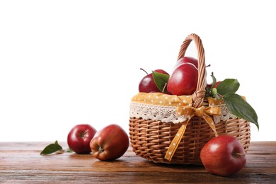 Photo of Ripe red apples in wicker basket on wooden table against white background. Space for text