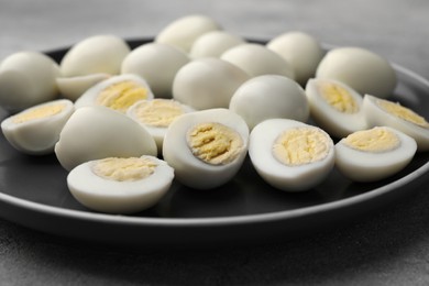 Photo of Plate with many peeled hard boiled quail eggs on grey table, closeup