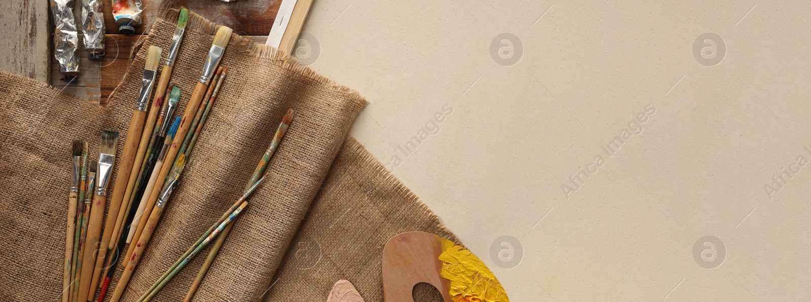 Photo of Natural burlap fabric and different painting supplies on beige background, top view