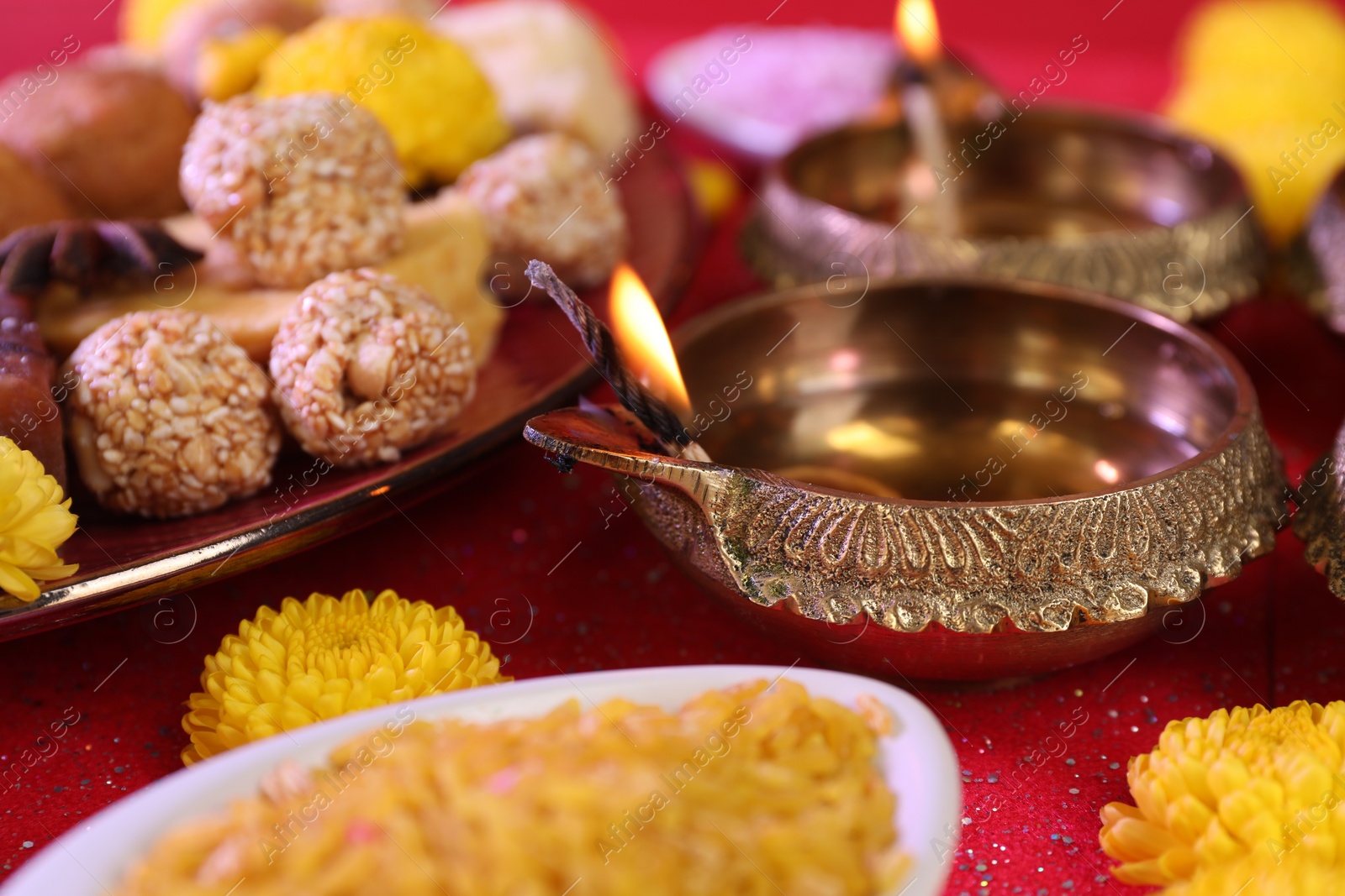 Photo of Diwali celebration. Diya lamps and tasty Indian sweets on shiny red table, closeup