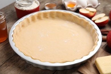 Photo of Raw dough for traditional English apple pie on wooden table, closeup