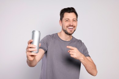 Photo of Happy man holding tin can with beverage on light grey background