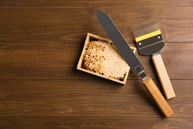 Photo of Honeycomb frame and beekeeping tools on wooden table, flat lay. Space for text