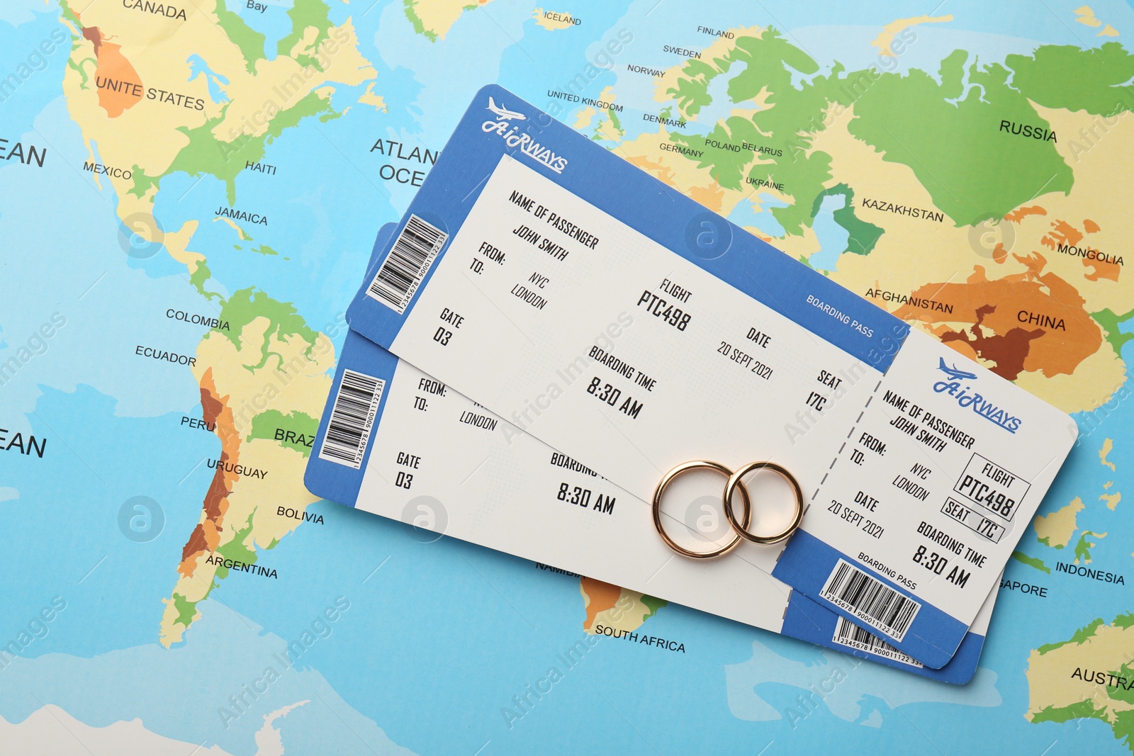 Photo of Honeymoon concept. Plane tickets and golden rings on world map, top view