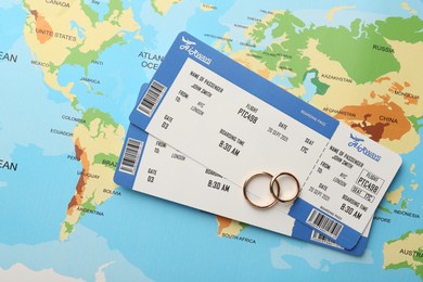 Honeymoon concept. Plane tickets and golden rings on world map, top view