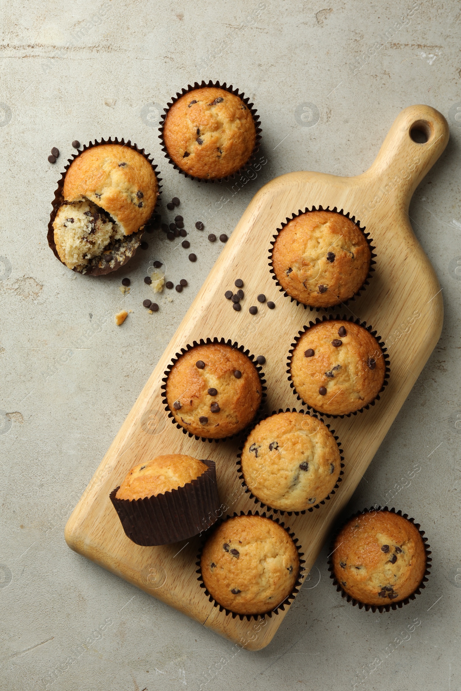 Photo of Delicious sweet muffins with chocolate chips on grey textured table, flat lay