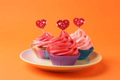 Photo of Delicious cupcakes with bright cream and heart toppers on orange background