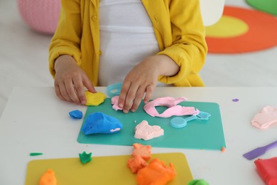 Photo of Little girl sculpting with play dough at table indoors, closeup