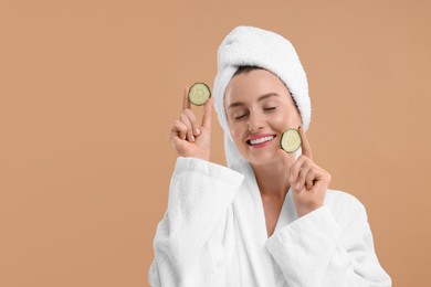 Photo of Beautiful woman in bathrobe with pieces of cucumber on beige background, space for text