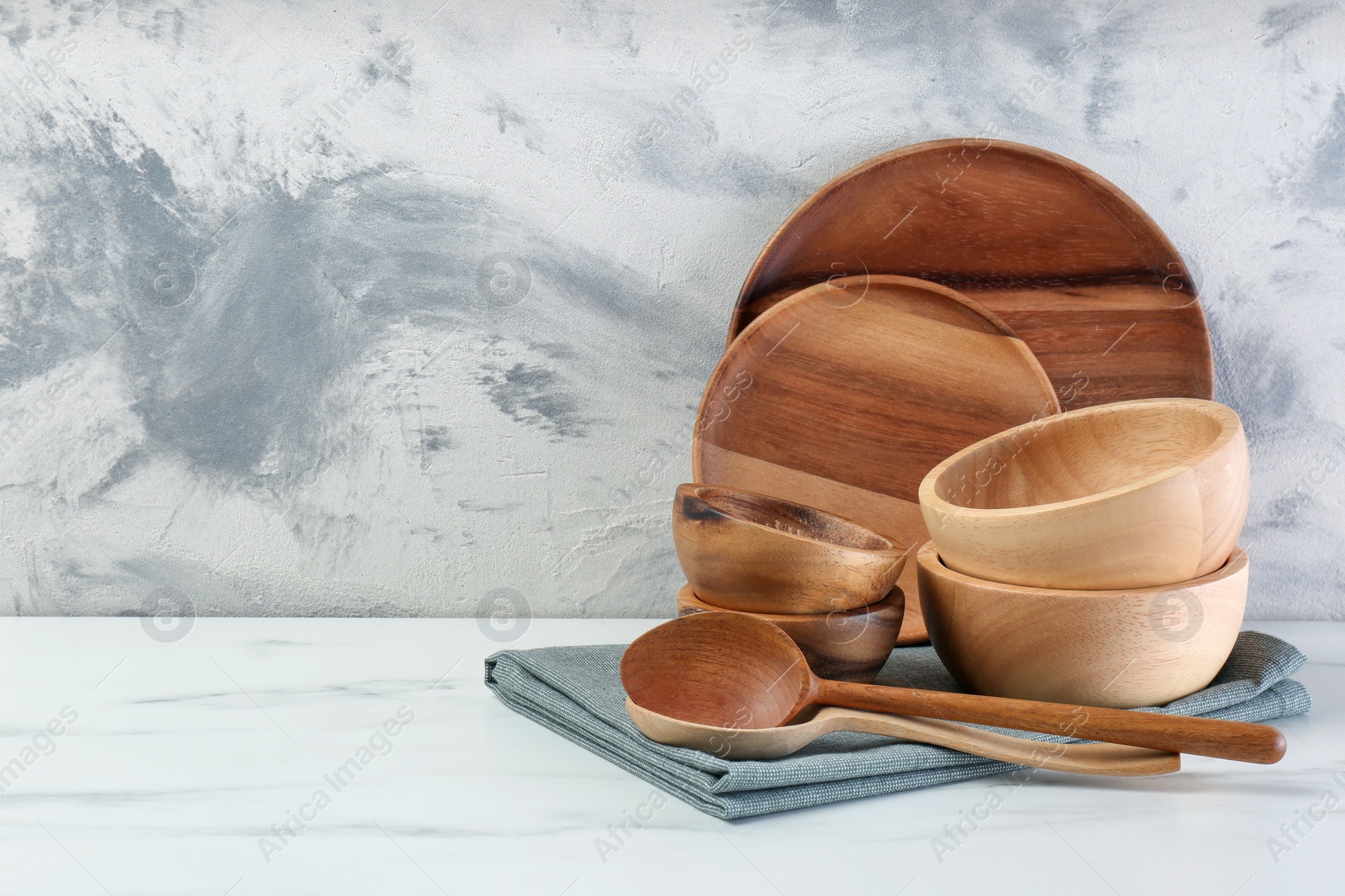 Photo of Set of wooden tableware on white marble table against textured wall. Space for text