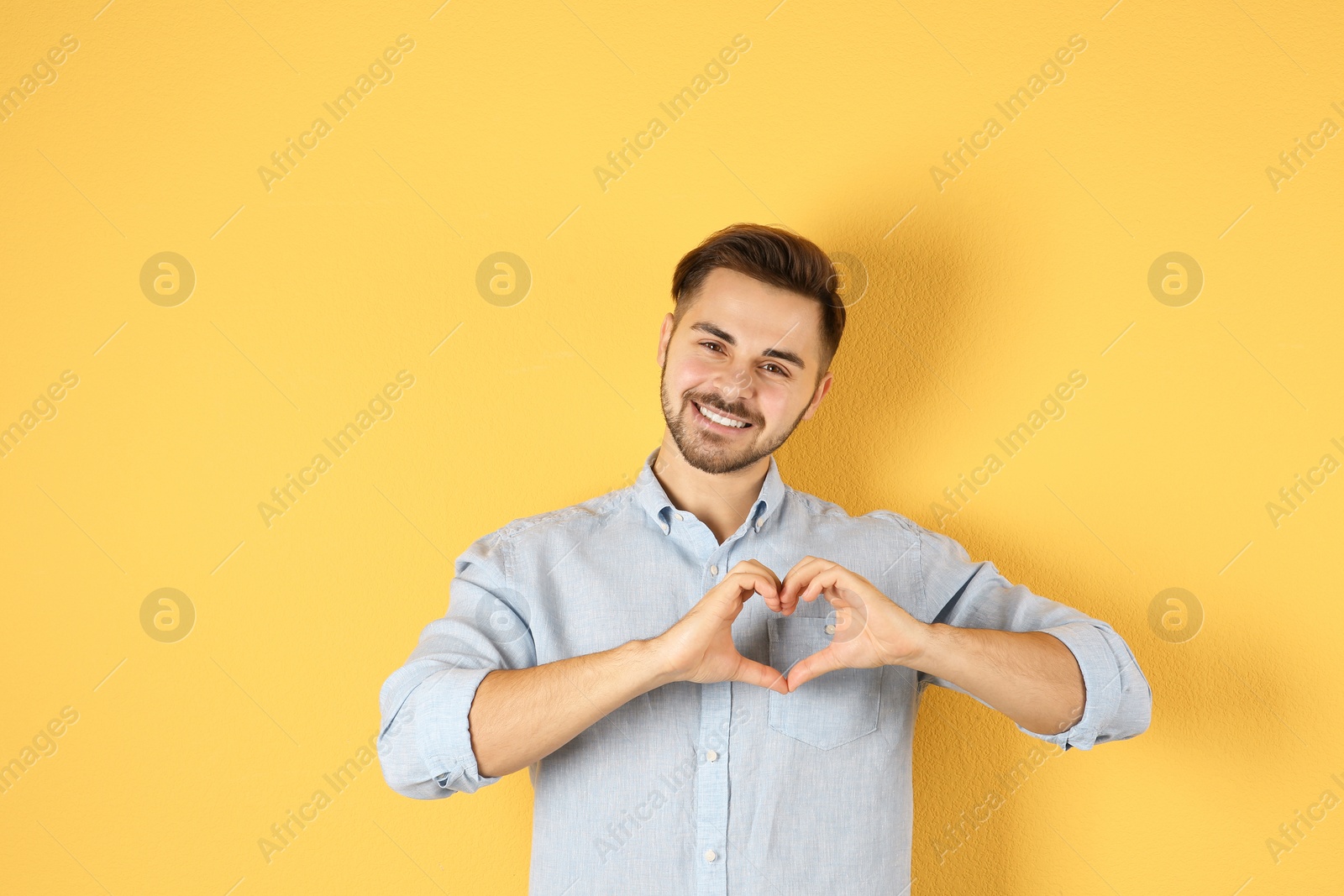 Photo of Portrait of young man making heart with his hands on color background