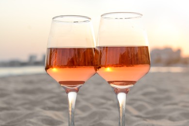 Photo of Glasses of tasty rose wine on sandy beach, closeup