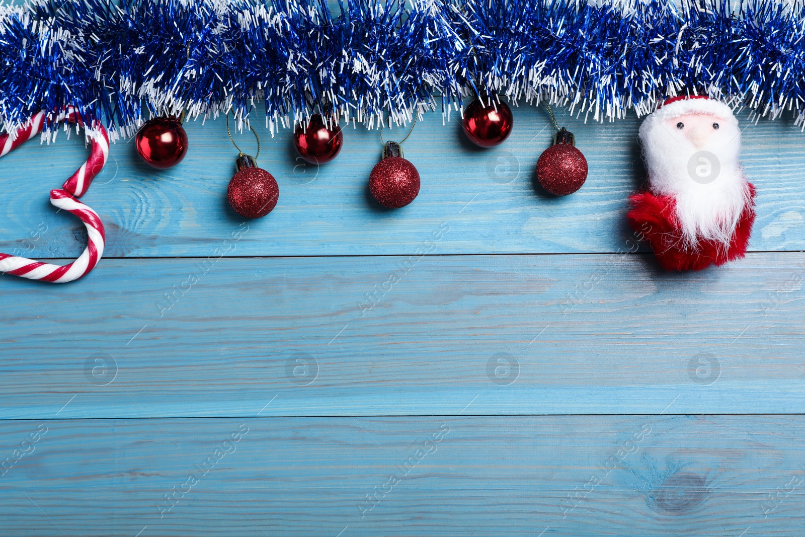 Photo of Bright tinsel, toy Santa and Christmas balls on light blue wooden background, flat lay. Space for text