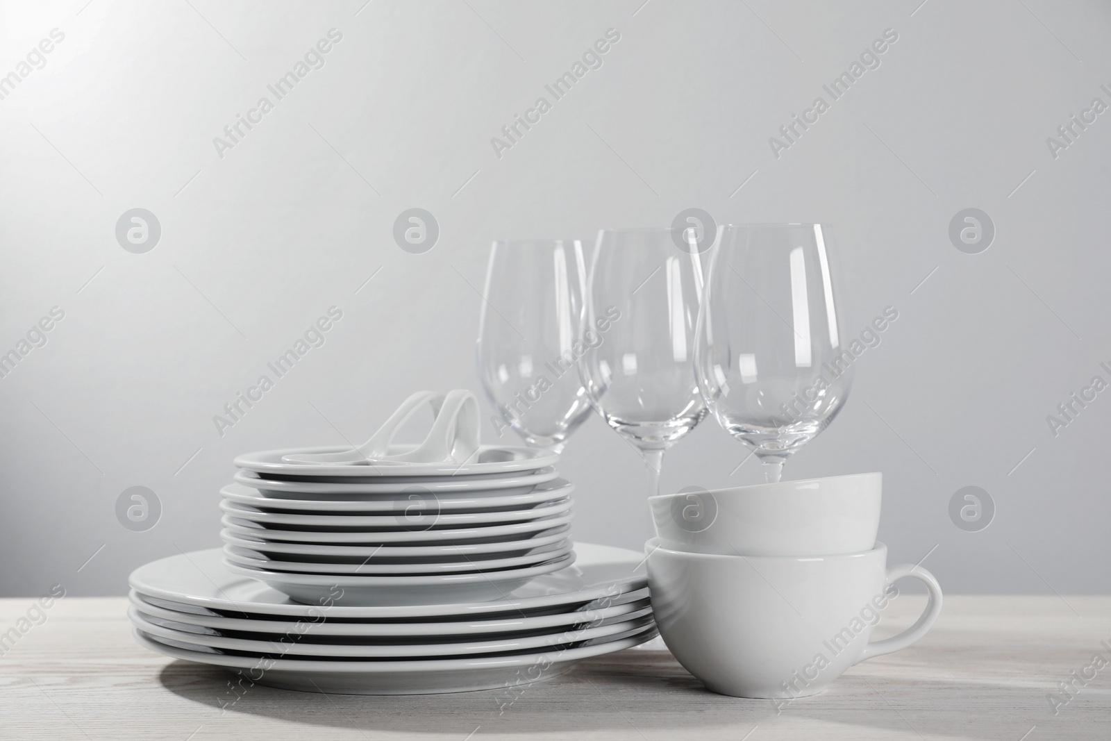 Photo of Set of clean dishware and glasses on white wooden table against light background