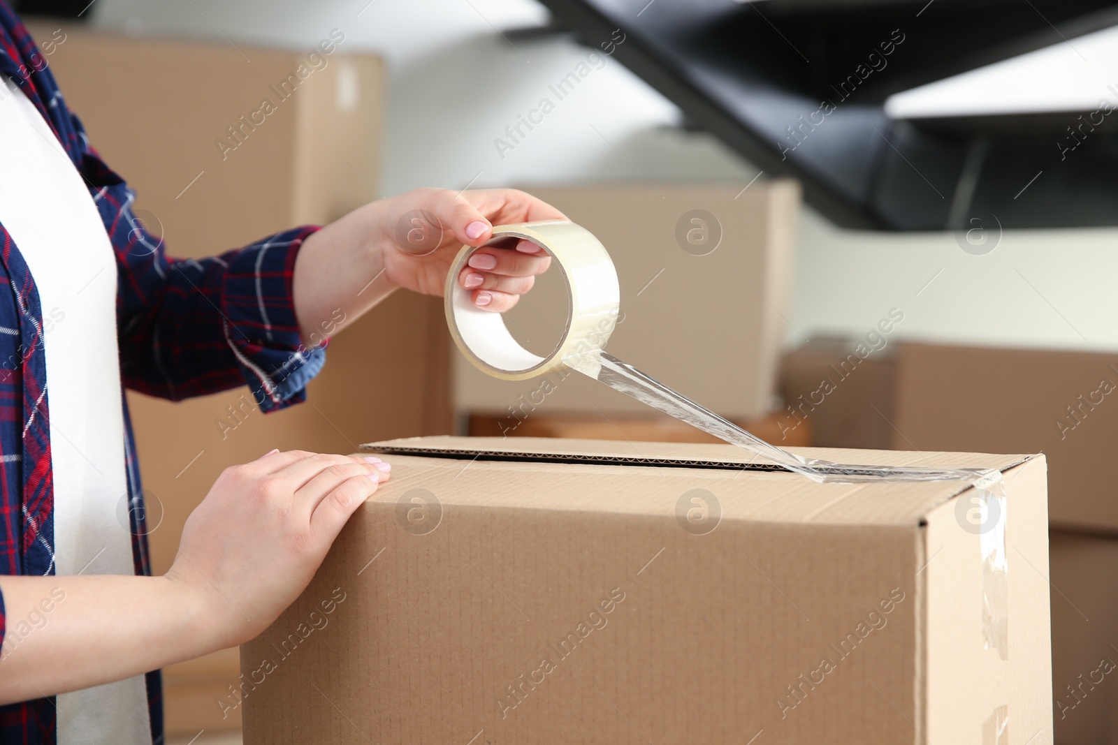 Photo of Woman taping cardboard box indoors, closeup. Moving day