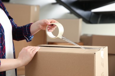 Photo of Woman taping cardboard box indoors, closeup. Moving day