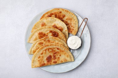 Photo of Delicious fried chebureki with cheese and sauce on light grey table, top view
